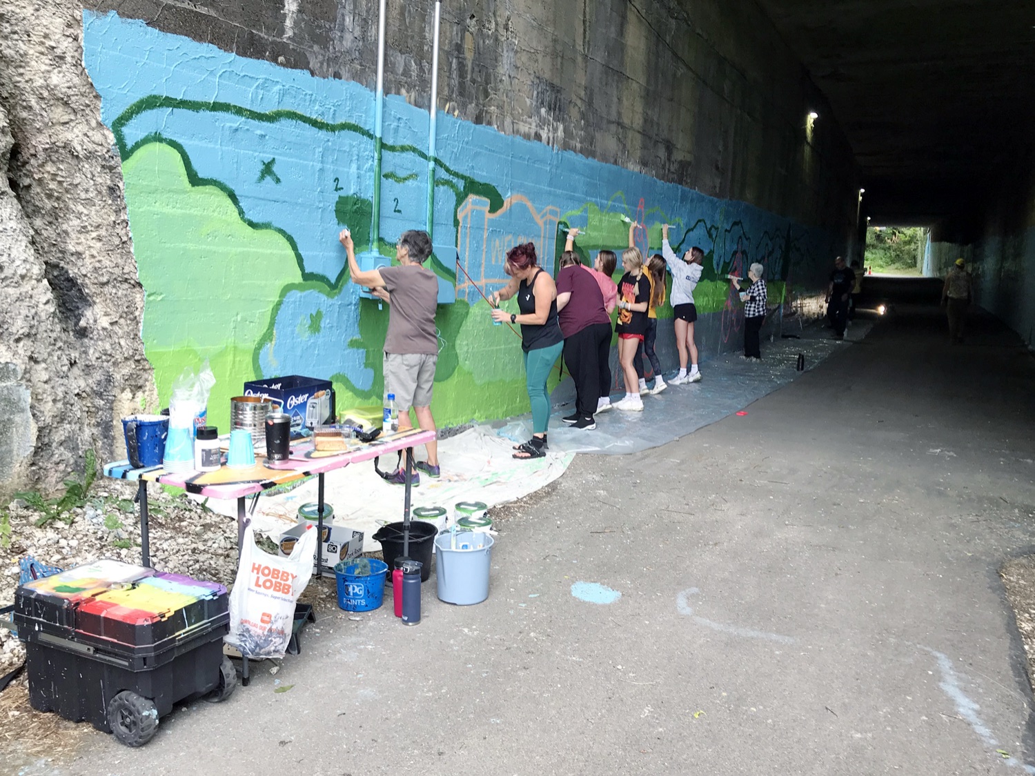 A long line of TrailKeeper volunteers painting a landscape mural on a tunnel wall along the Five Star Trail